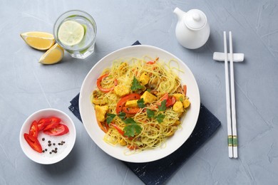 Photo of Stir-fry. Delicious cooked noodles with chicken and vegetables in bowl served on gray textured table, flat lay