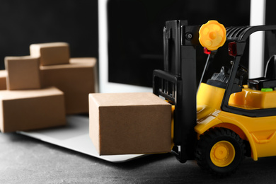 Toy forklift with box near laptop on table. Logistics and wholesale concept