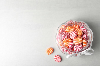 Photo of Sweet candies in glass jar on light grey table, flat lay. Space for text
