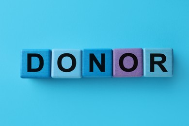 Photo of Word Donor made of cubes on light blue background, top view