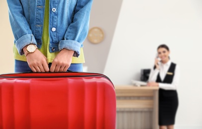Image of Woman with suitcase near receptionist in hotel, closeup view