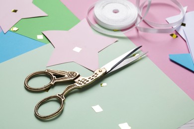 Photo of Pair of scissors near ribbon on colorful paper sheets, closeup