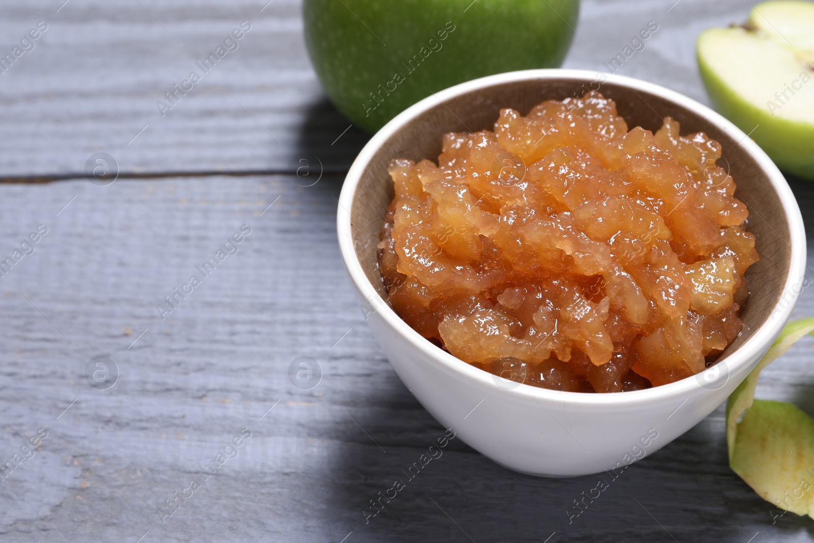 Photo of Delicious apple jam in bowl and fresh fruits on grey wooden table, closeup. Space for text