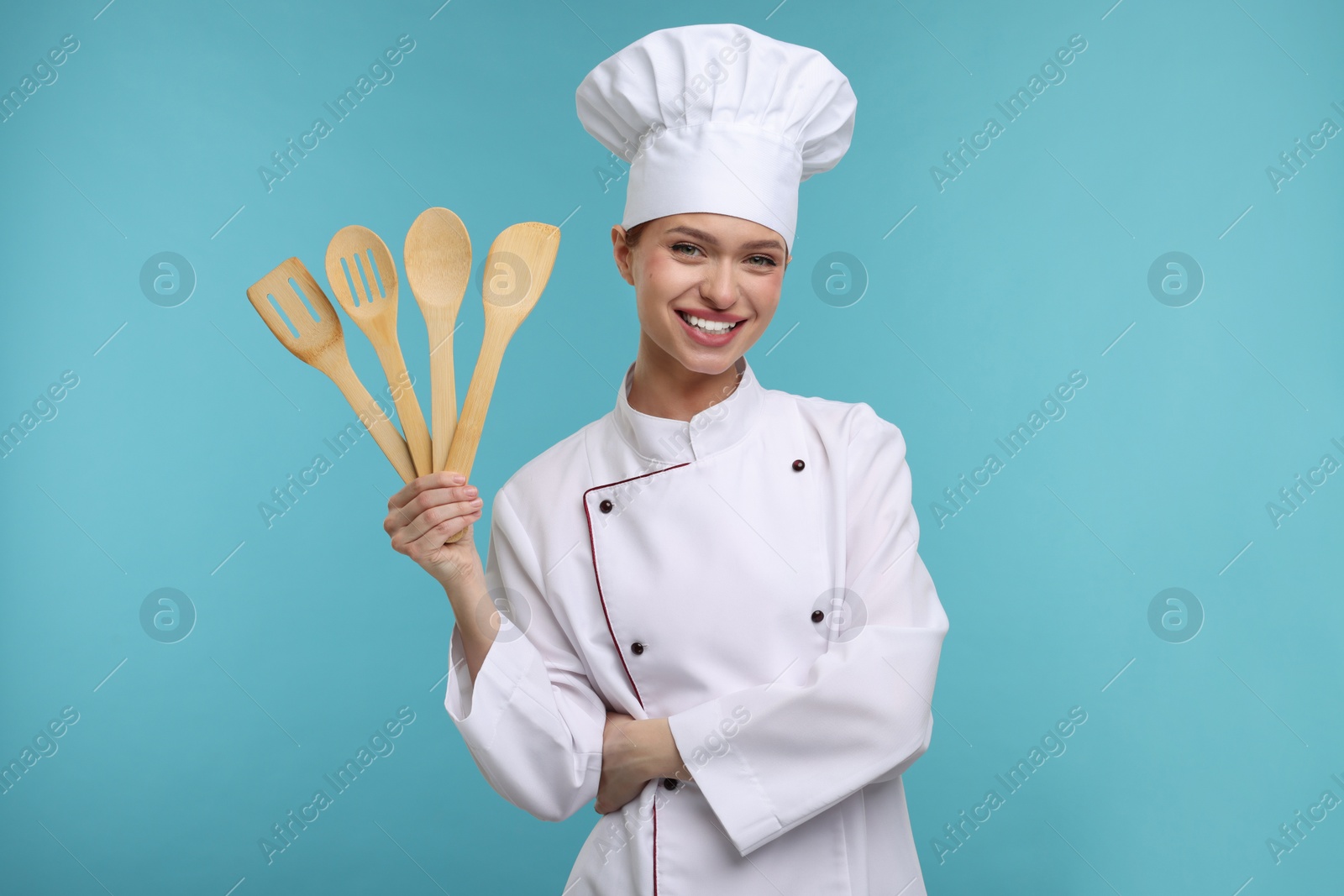 Photo of Happy chef in uniform holding wooden utensils on light blue background