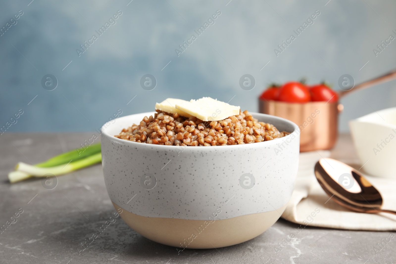 Photo of Bowl of buckwheat porridge with butter on grey marble table