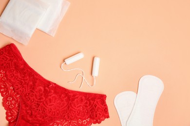 Flat lay composition with woman's underwear and menstrual pads on pale orange background, space for text
