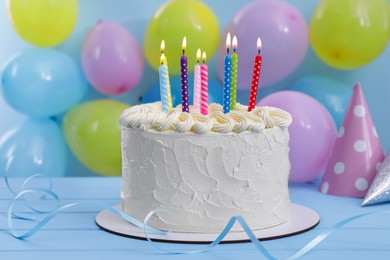 Photo of Delicious cake with burning candles and festive decor on light blue background