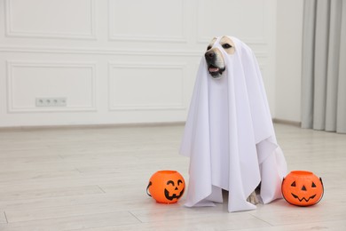 Photo of Cute Labrador Retriever dog wearing ghost costume with Halloween buckets indoors. Space for text
