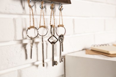 Photo of Holder with different keys on white brick wall indoors, closeup