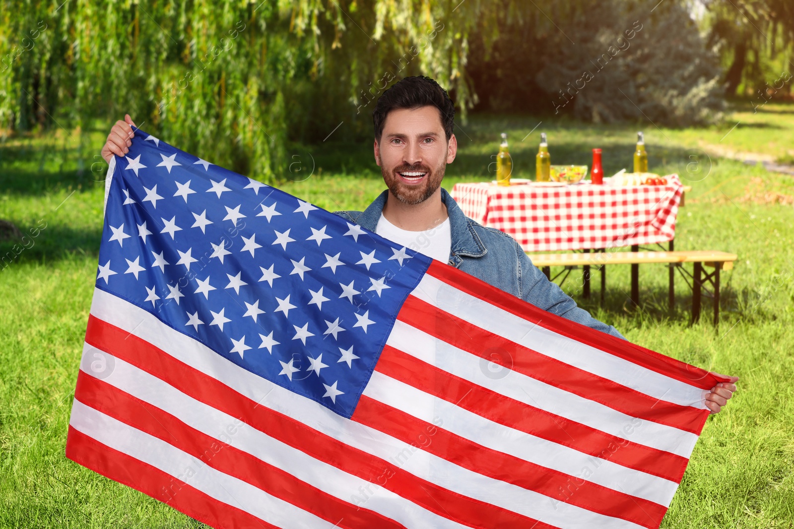 Image of 4th of July - Independence day of America. Happy man with national flag of United States having picnic in park