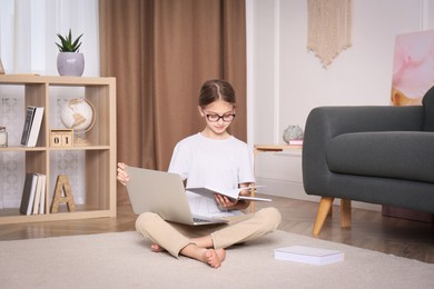 Girl with laptop and books sitting on floor at home
