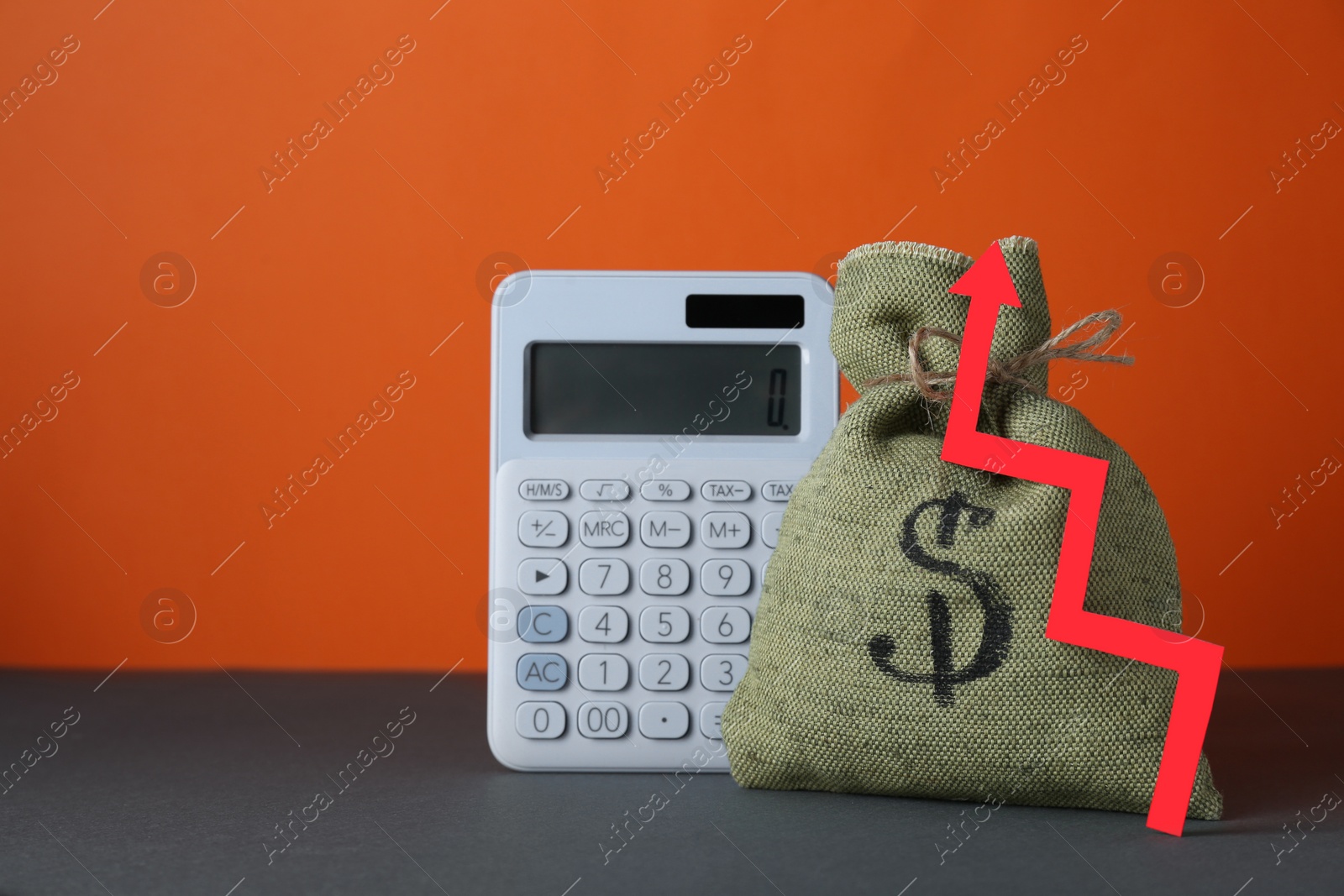 Photo of Economic profit. Money bag, calculator and arrow on grey table against orange background, space for text