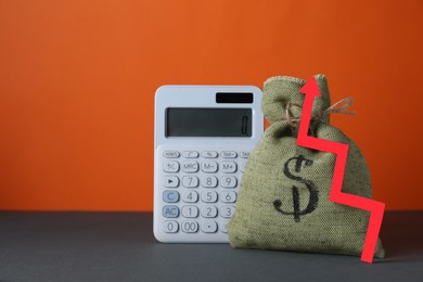 Photo of Economic profit. Money bag, calculator and arrow on grey table against orange background, space for text