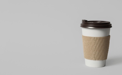 Photo of Takeaway paper coffee cup with cardboard sleeve on light grey background. Space for text