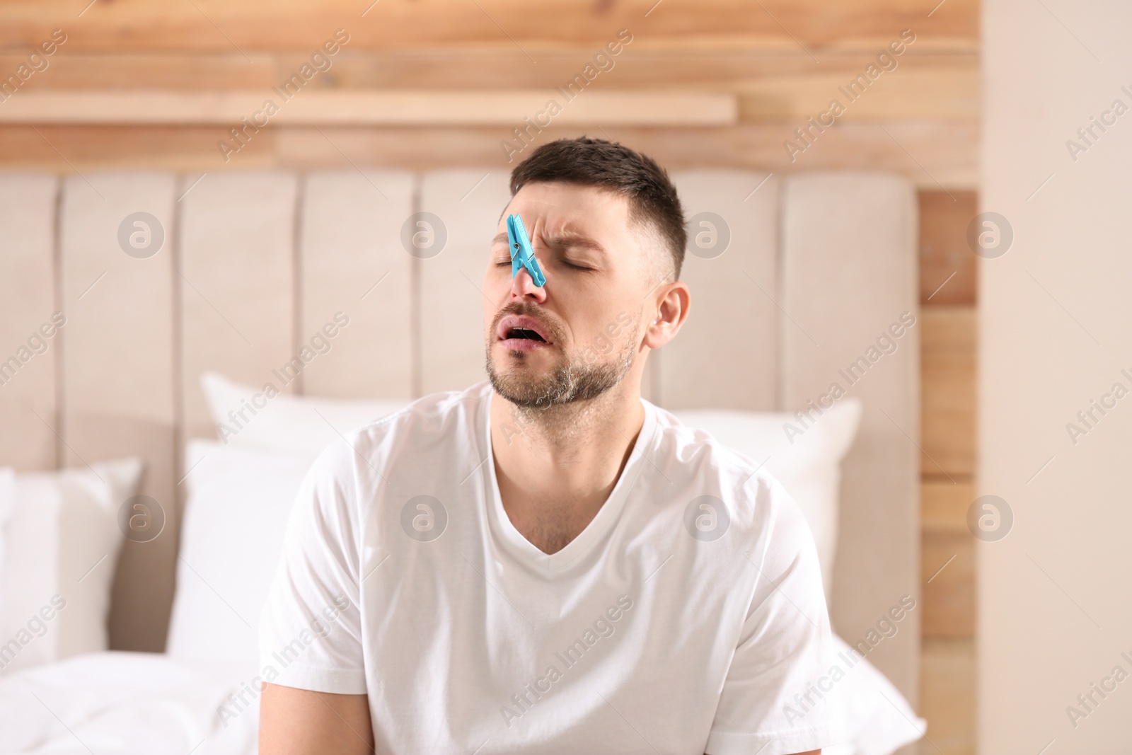 Photo of Man with clothespin suffering from runny nose in bedroom