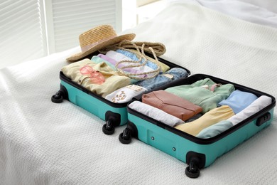Photo of Open suitcase packed for trip and accessories on bed