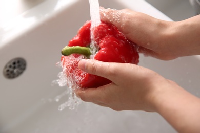 Woman washing fresh bell pepper in kitchen sink, closeup