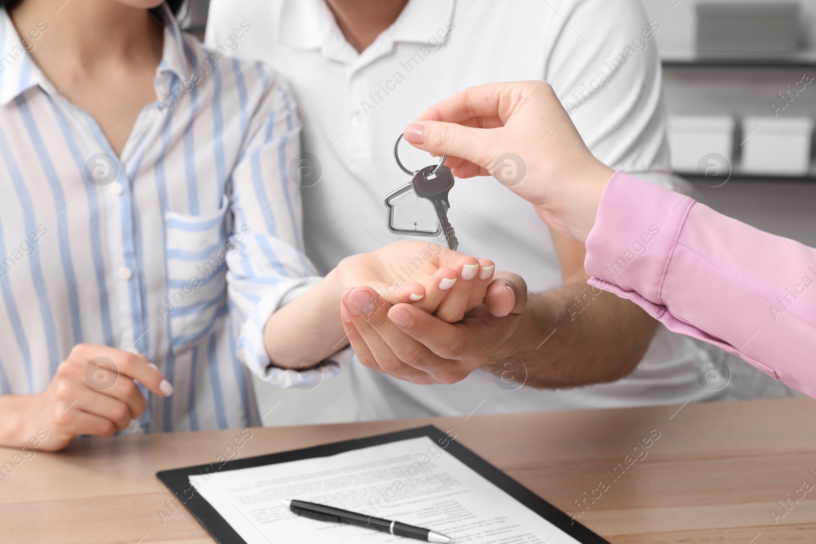 Photo of Real estate agent giving house key to couple at table in office, closeup