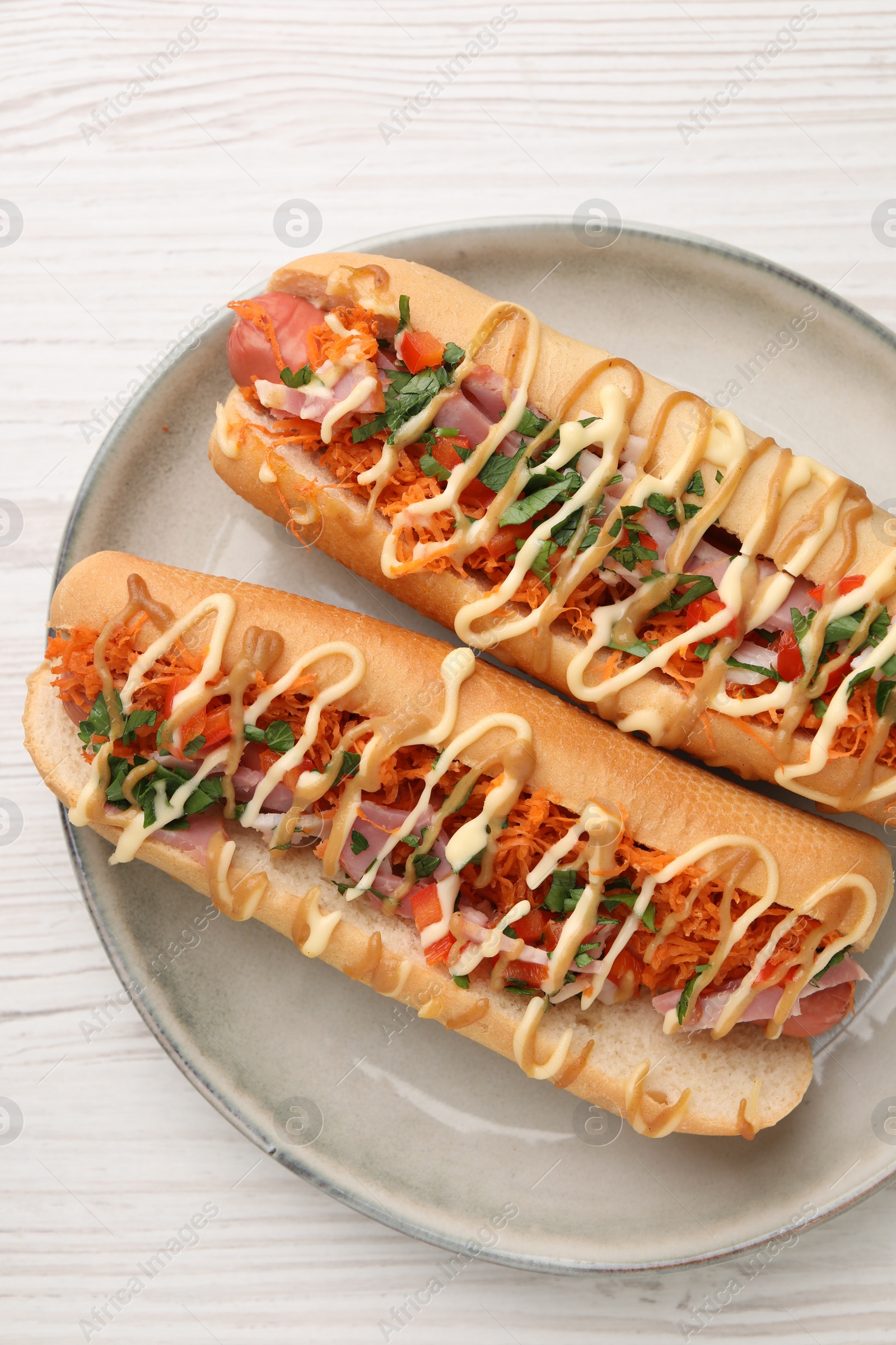 Photo of Delicious hot dogs with bacon, carrot and parsley on white wooden table, top view