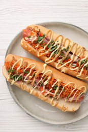 Delicious hot dogs with bacon, carrot and parsley on white wooden table, top view