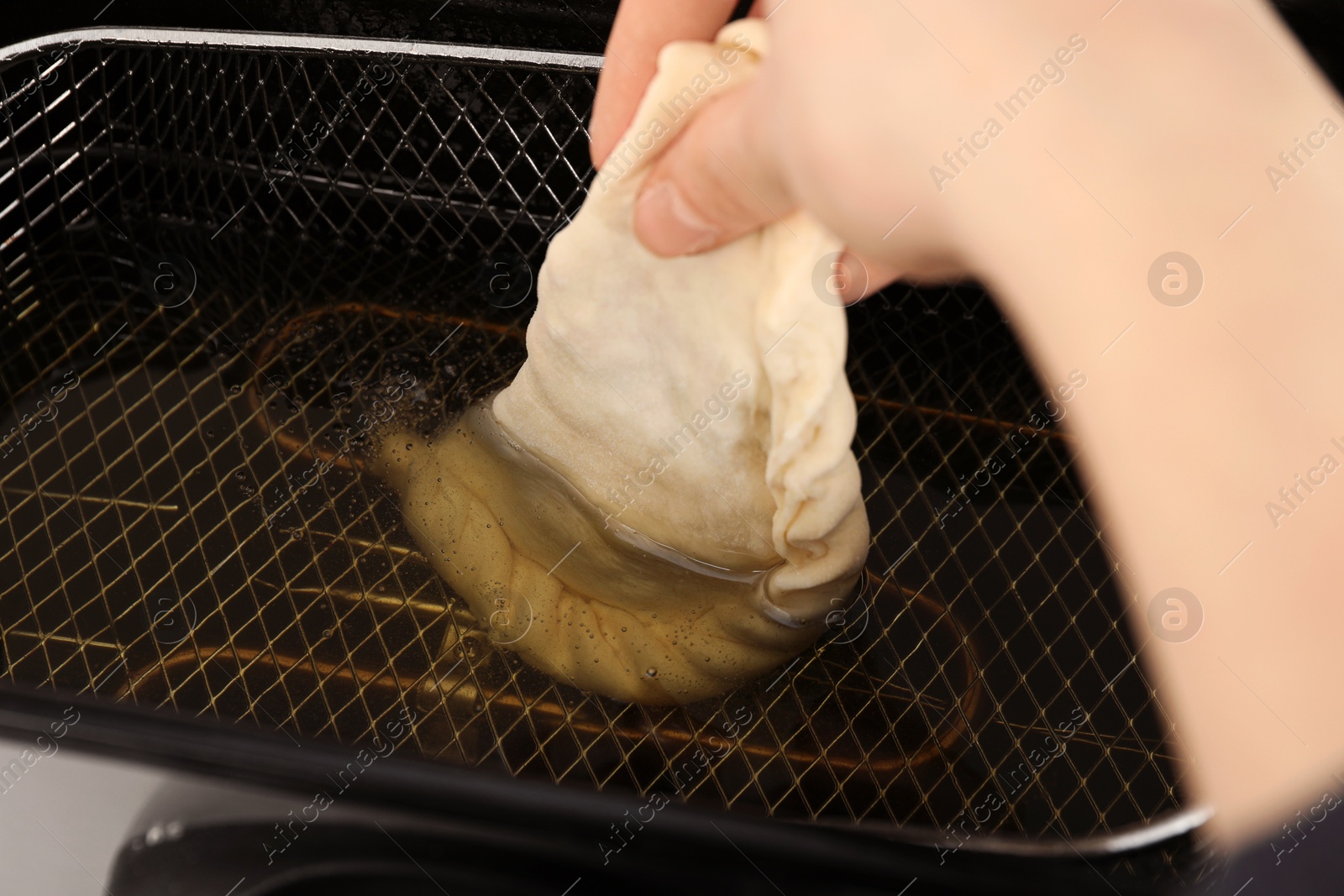 Photo of Woman frying chebureki with tasty filling in deep fryer, closeup