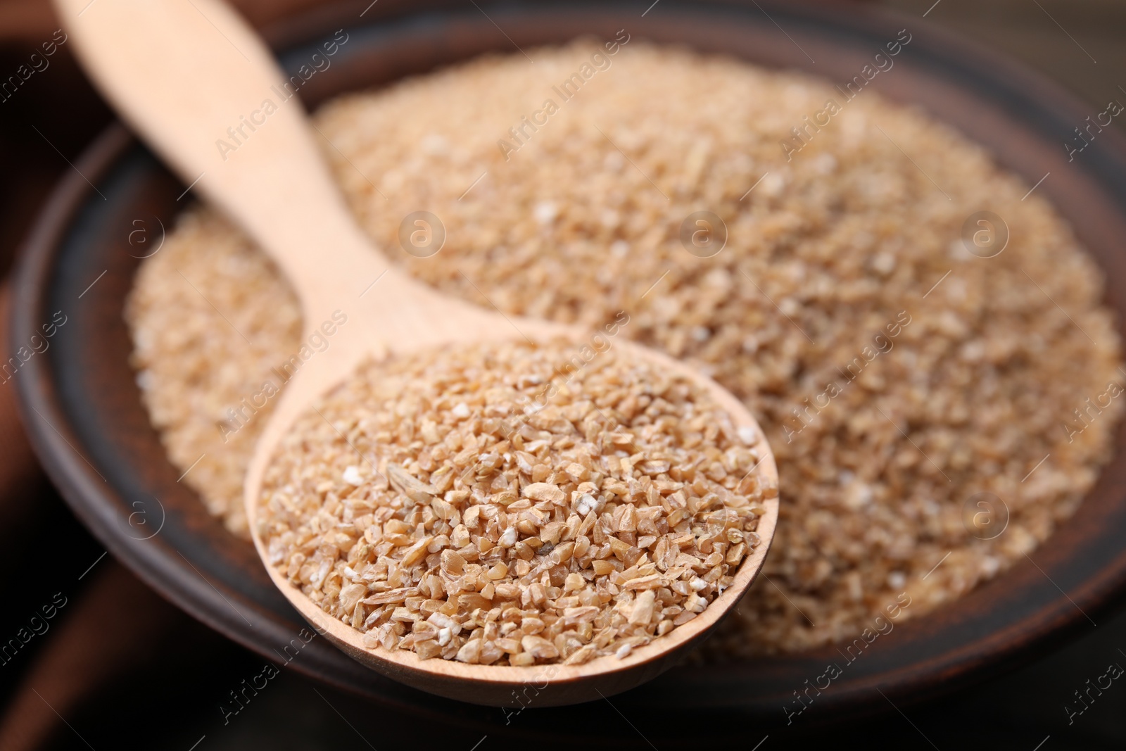 Photo of Dry wheat groats in bowl and spoon, closeup