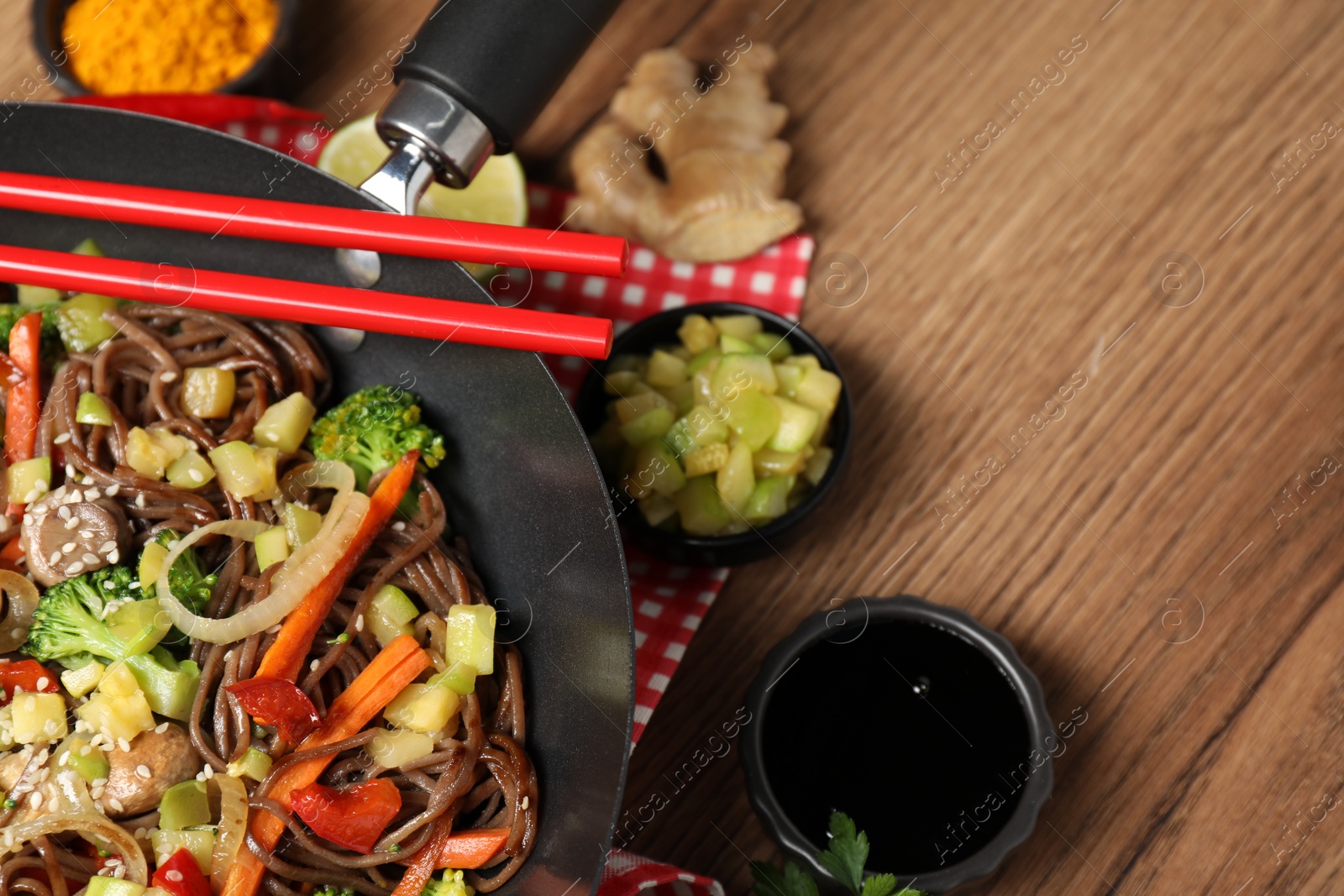 Photo of Stir-fry. Tasty noodles with meat in wok, chopsticks and ingredients on wooden table, closeup