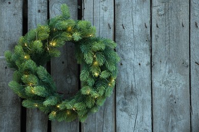 Photo of Beautiful Christmas wreath with string lights hanging on wooden wall, space for text