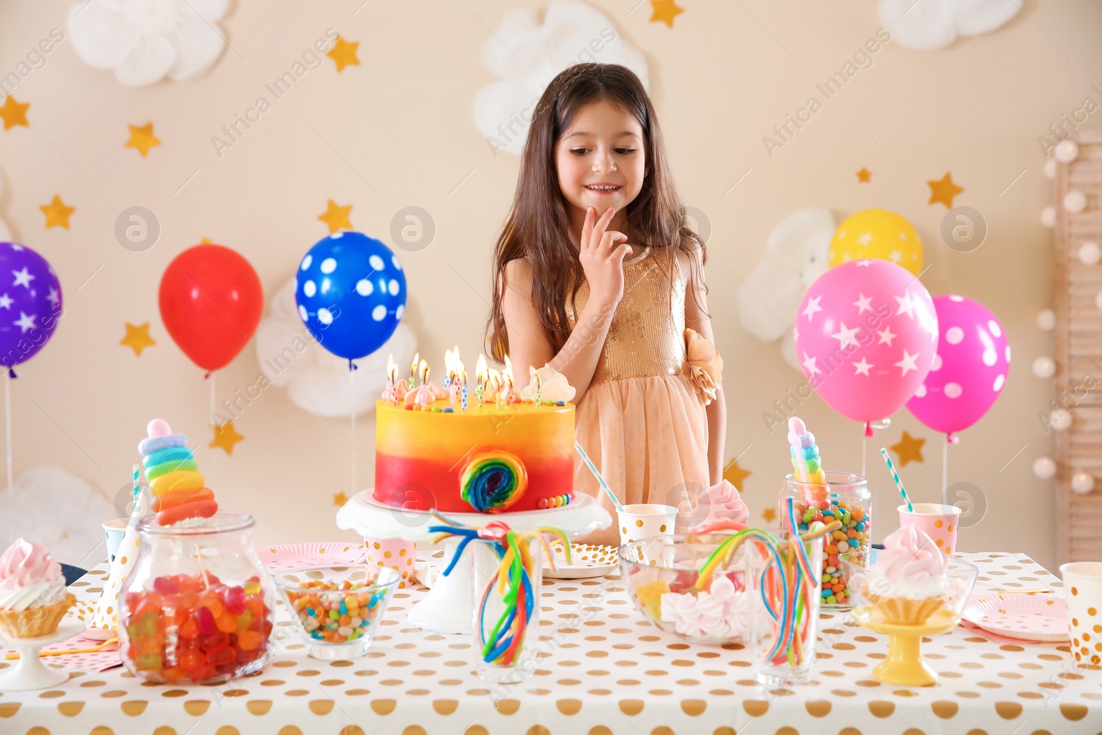 Photo of Cute little girl making wish before blowing out candles on her birthday cake indoors