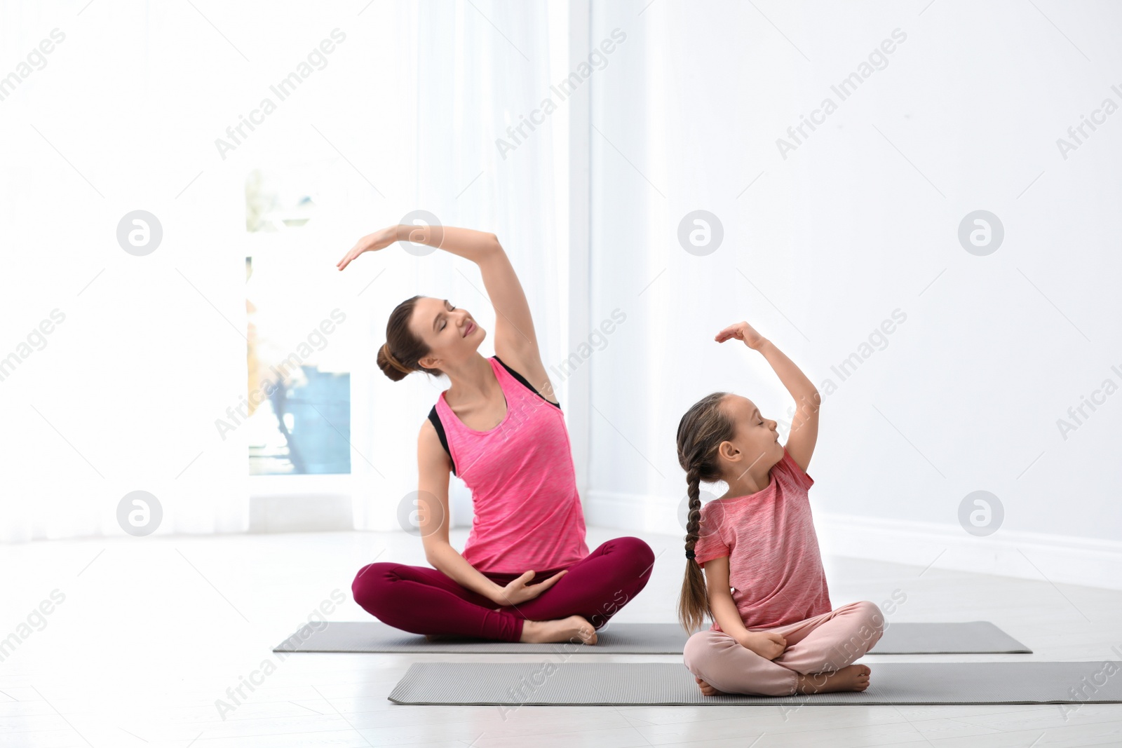 Photo of Young mother with little daughter practicing yoga at home