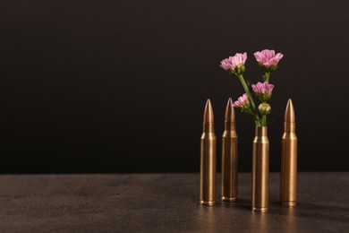 Bullets and cartridge case with beautiful flowers on grey table against dark background. Space for text