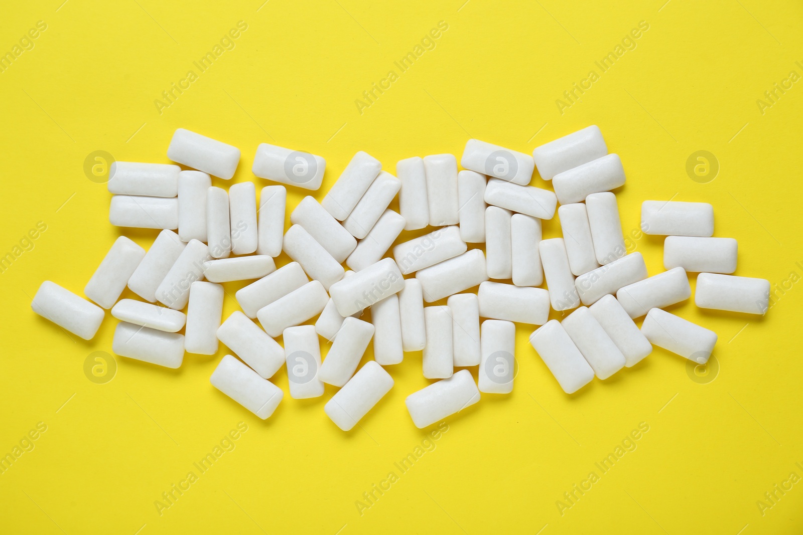 Photo of Tasty white chewing gums on yellow background, flat lay