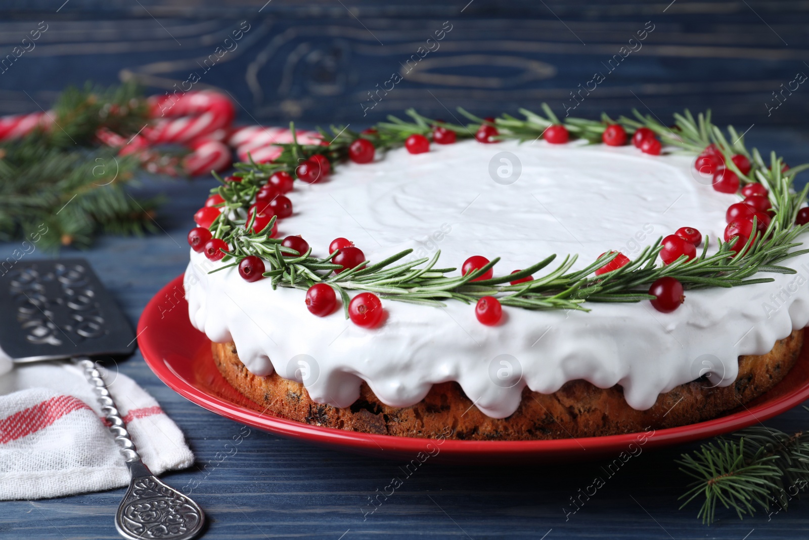 Photo of Traditional Christmas cake decorated with rosemary and cranberries on blue wooden table, closeup