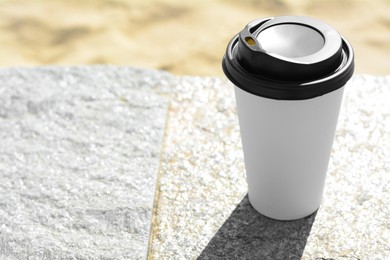 Photo of Takeaway coffee cup on stone surface outdoors. Space for text