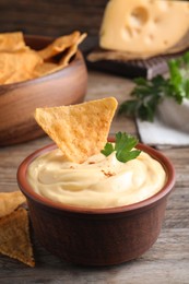 Photo of Delicious cheese sauce with nacho and parsley on wooden table