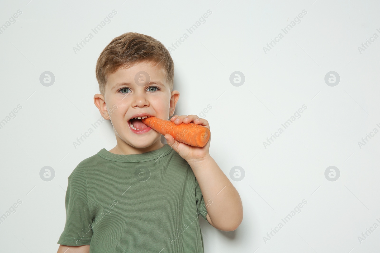 Photo of Adorable little boy eating carrot on white background. Space for text
