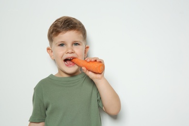 Adorable little boy eating carrot on white background. Space for text