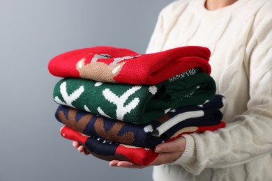 Photo of Woman holding stack of different Christmas sweaters on grey background, closeup