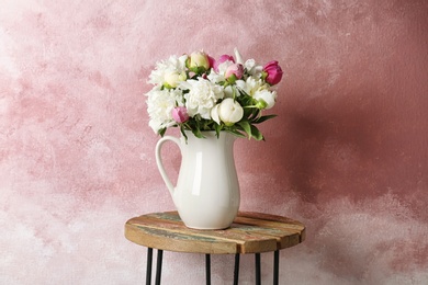 Photo of Vase with bouquet of beautiful flowers on table against color background