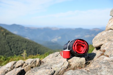 Photo of Sleeping bag and cup on mountain peak, space for text