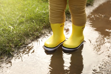 Little girl wearing rubber boots standing in puddle, closeup