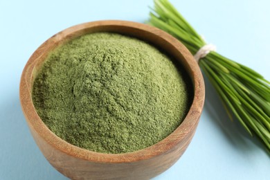 Wheat grass powder in bowl and fresh sprouts on light blue background, closeup