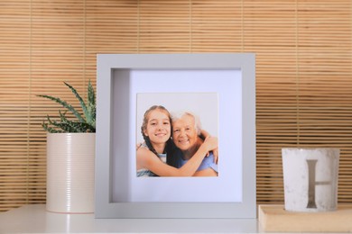 Photo of Frame with photo of elderly woman and her granddaughter on white table indoors