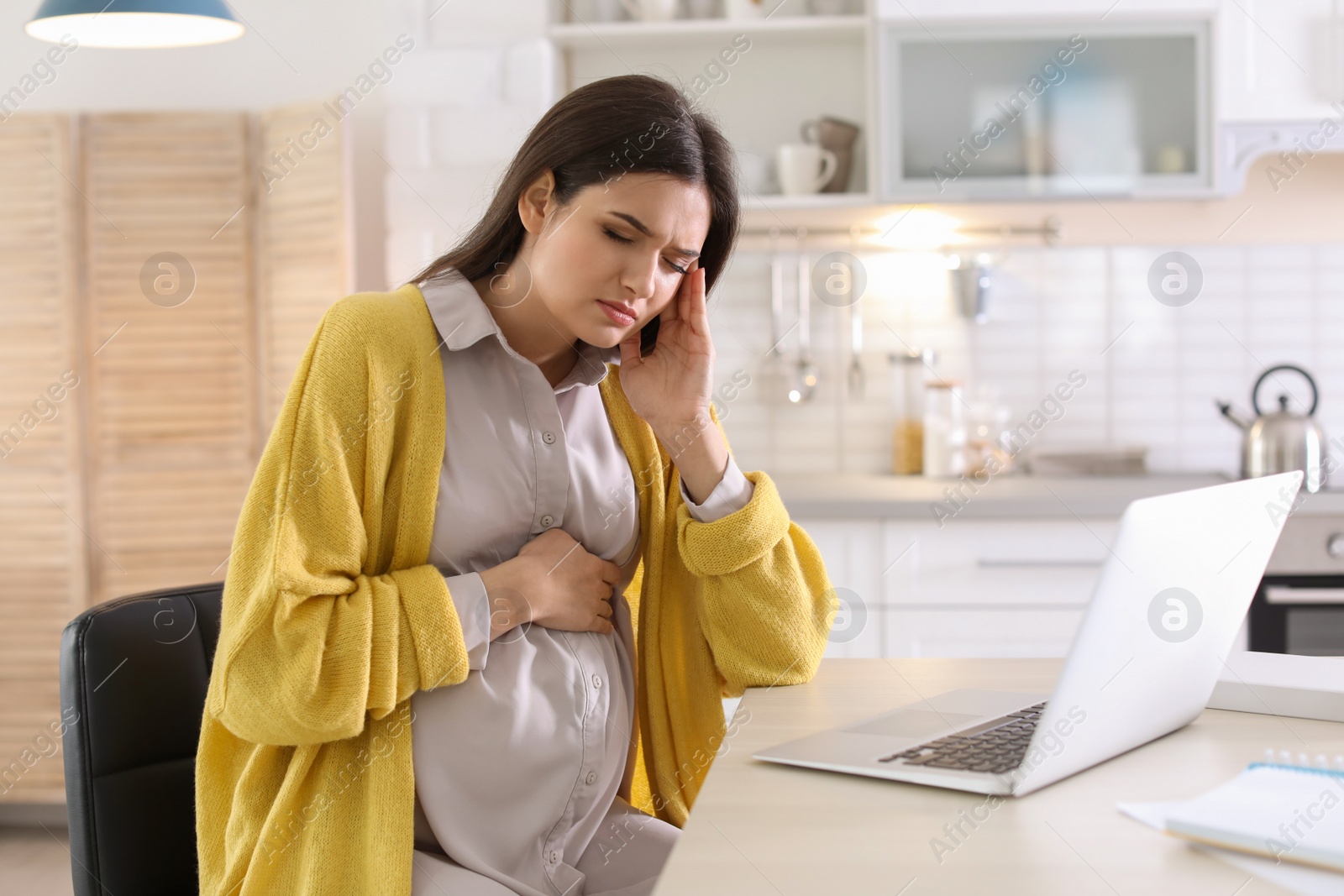 Photo of Young pregnant woman suffering from headache in home office