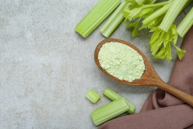 Photo of Natural celery powder in wooden spoon and fresh stalks on grey table, flat lay. Space for text