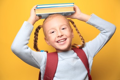 Photo of Cute little girl with textbooks and backpack on yellow background