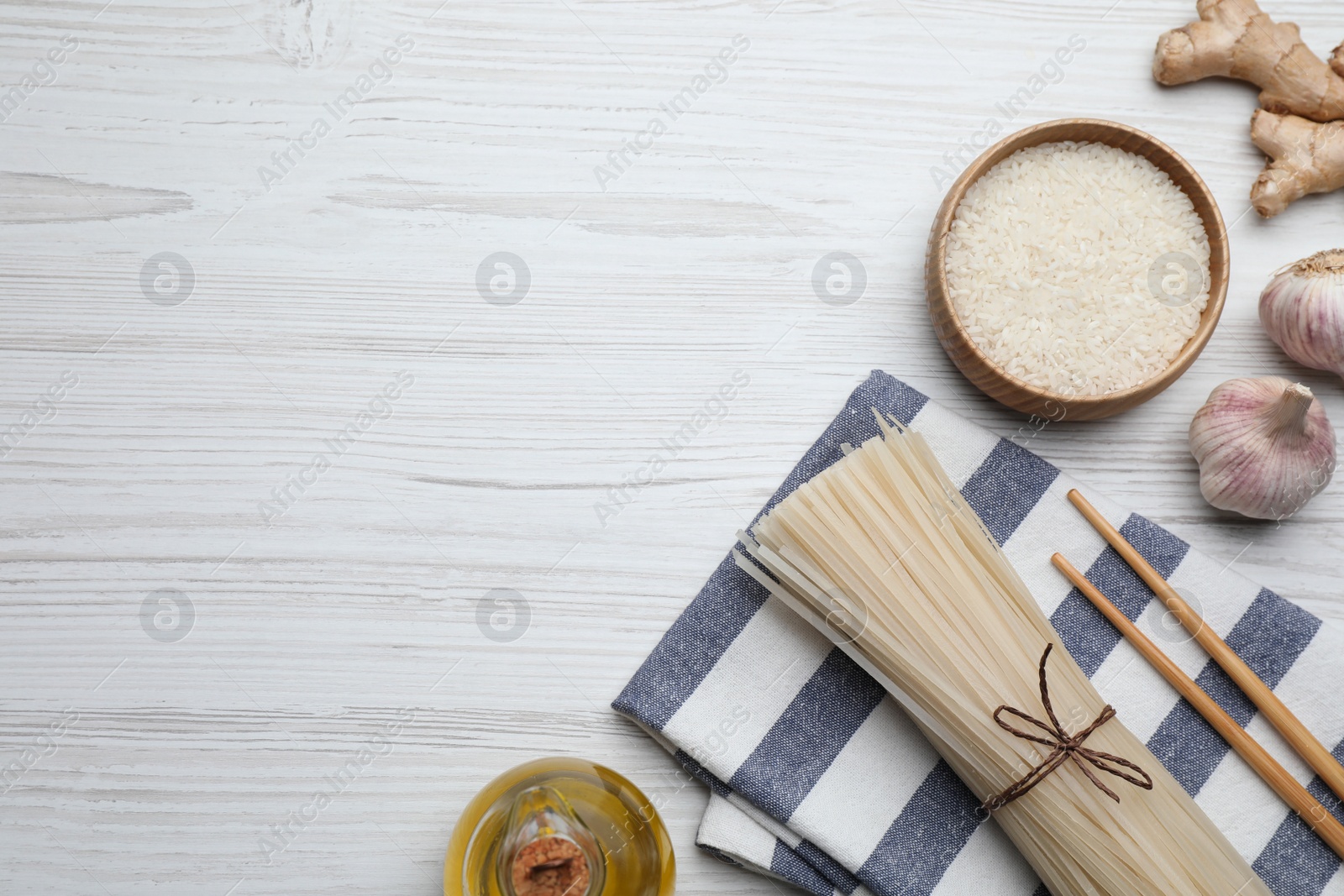 Photo of Bowl with dried rice noodles and ingredients on white wooden table, flat lay. space for text