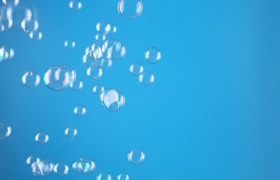 Beautiful transparent soap bubbles on light blue background, space for text