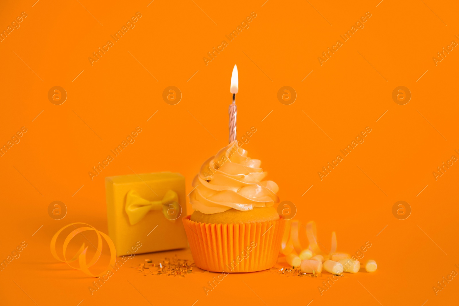 Image of Delicious birthday cupcake with burning candle, marshmallows and gift box on orange background
