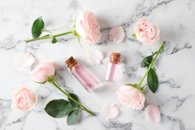 Photo of Flat lay composition with rose essential oil and flowers on marble table